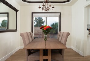 Un comedor con una mesa de madera y sillas acolchadas, un florero con flores y una araña.