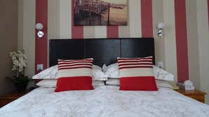 A hotel room with a bed, striped walls, a painting of a waterfront, and a potted plant. - Lansdowne hotel (Royal Leamington Spa)