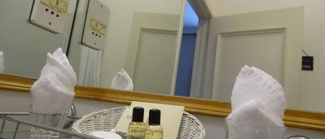 A bathroom with a glass partition, a mirror, a basket with toiletries, and a towel dispenser.
