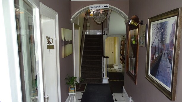 A hallway with a reception sign, a staircase, and a framed painting on the wall. - Lansdowne hotel (Royal Leamington Spa)