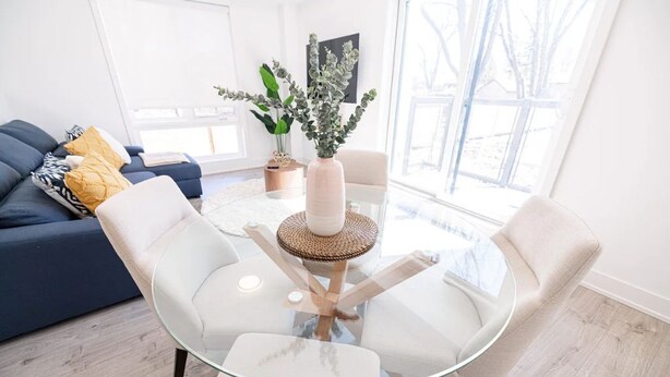 A modern living room with a glass coffee table, white chairs, a blue sofa, and a potted plant.