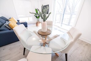 A modern living room with a glass coffee table, white chairs, a blue sofa, and a potted plant.