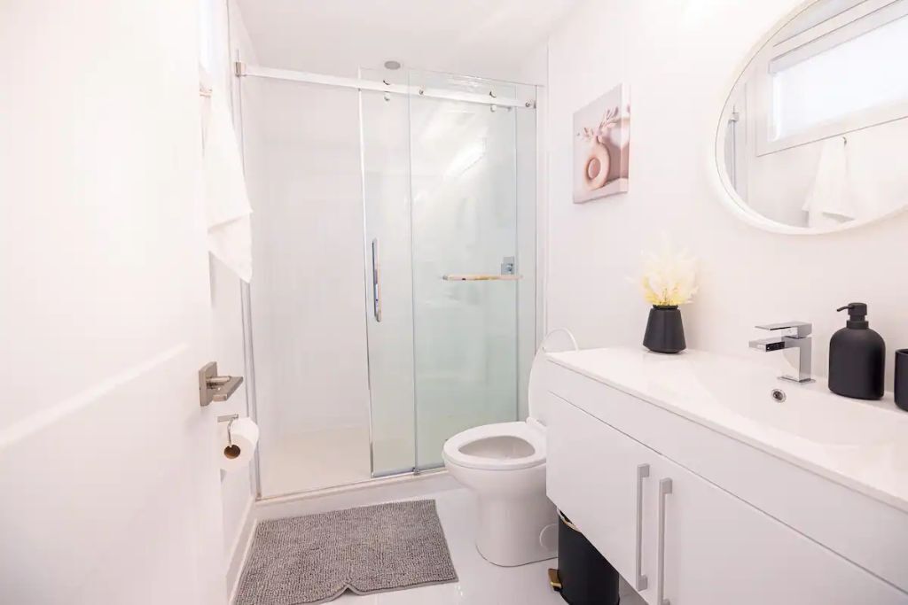 A modern bathroom with a glass shower enclosure, a white toilet, a vanity with a mirror, and a small potted plant.