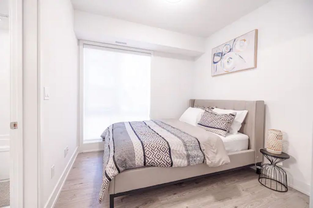 A bedroom with a bed, a window, and a wall-mounted artwork.