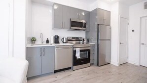 A compact kitchen with grey cabinets, a microwave, a refrigerator, and a dishwasher.
