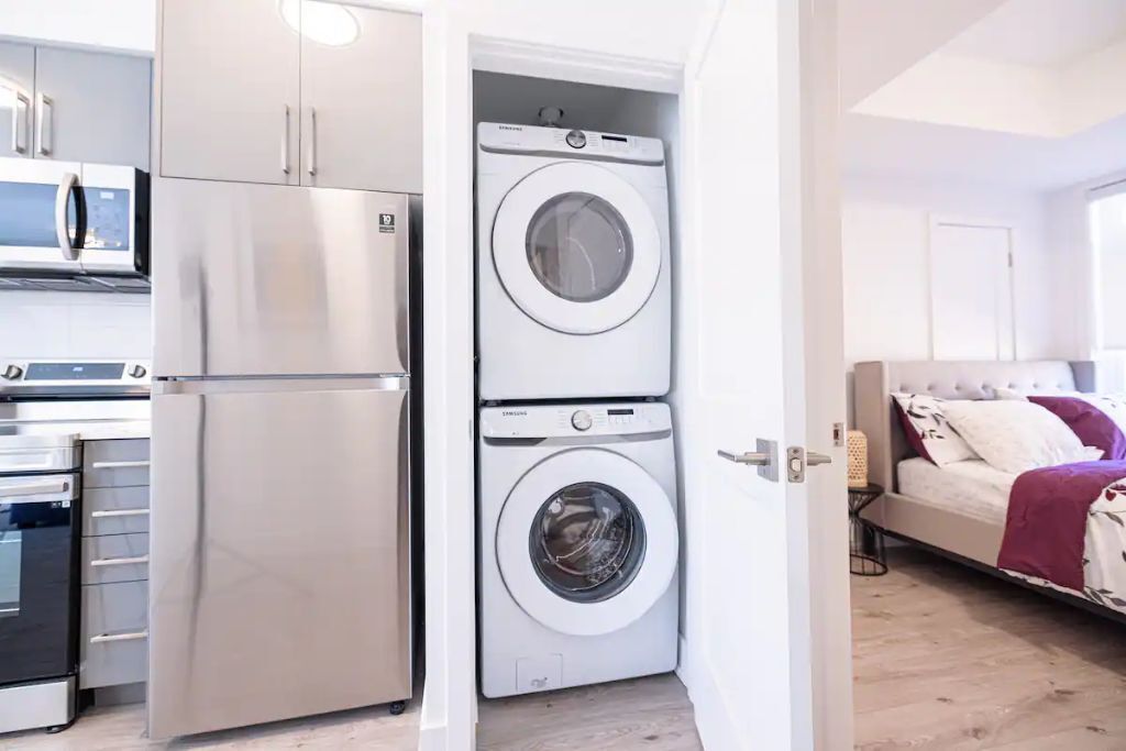 A compact kitchen with a refrigerator, microwave, and oven. There is a washing machine in the corner.