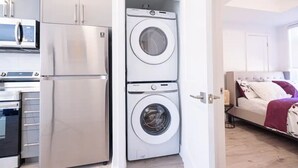 A compact kitchen with a refrigerator, microwave, and oven. There is a washing machine in the corner.