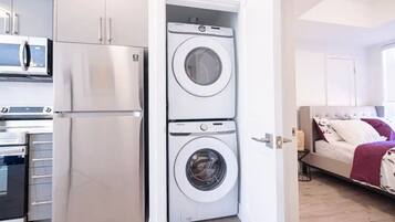 A compact kitchen with a refrigerator, microwave, and oven. There is a washing machine in the corner.