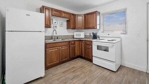 Cucina con mobili in legno, frigorifero bianco, forno a microonde, piano cottura e finestra con persiane.
