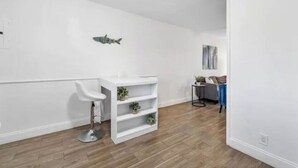 Una stanza moderna e minimalista con parete bianca, pavimento in legno, uno sgabello da bar bianco e una scaffalatura bianca con piante.
