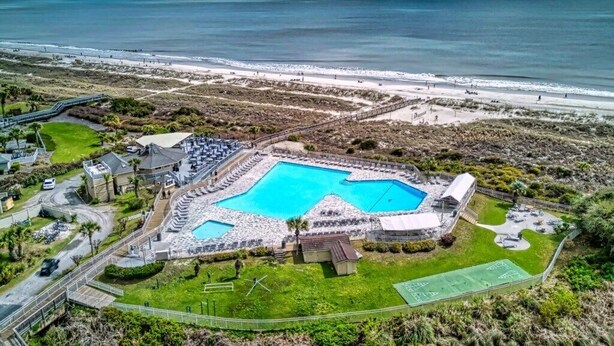 Ein Resort mit großem zentralen Pool, einem Strand und einem Tennisplatz.