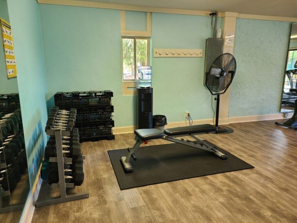 Une salle de sport équipée de matériel d’exercice, d’un distributeur d’eau et d’un ventilateur.