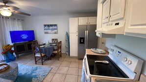 Eine kompakte Küche mit Kühlschrank, Backofen und Mikrowelle. Es gibt einen Essbereich mit Tisch und Stühlen, und im Hintergrund steht ein Fernseher.