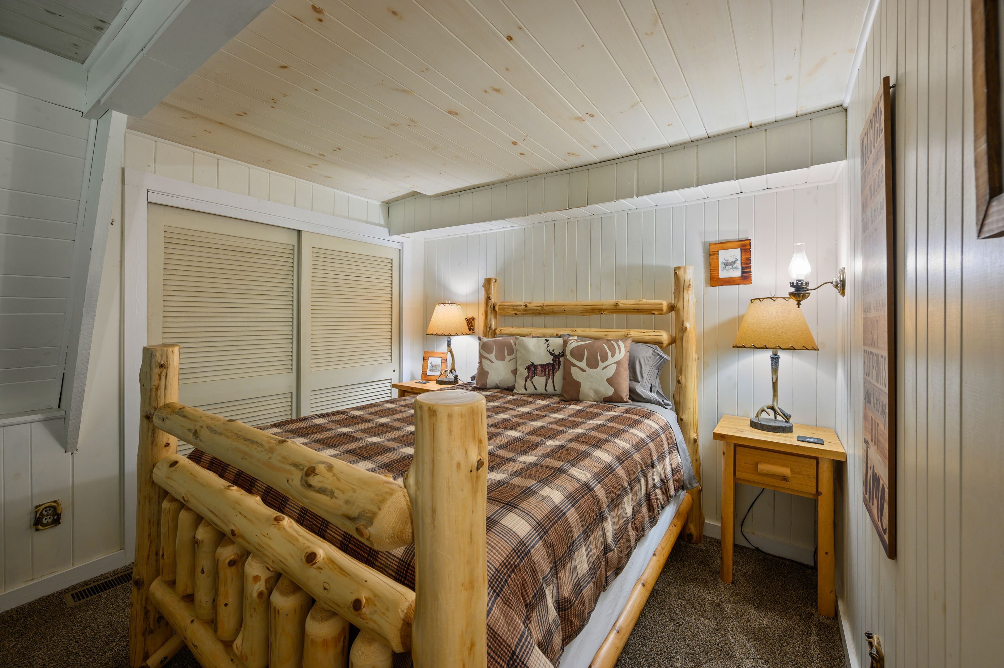 A wooden bed with a plaid bedspread, two bedside lamps, and a small wooden nightstand with a lamp.