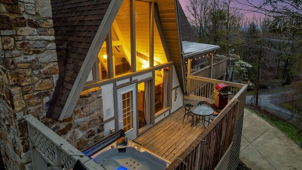 A cozy cabin with a stone exterior, a deck with a hot tub, and a view of the surrounding forest. - Mtn VIEWS, 4 bedrooms, hot tub, Arcade games, close to Ober + Gatlinburg (Gatlinburg)