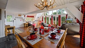 A dining area with a wooden table set for a meal, a chandelier, and a view of the outdoors through large windows. - Mtn VIEWS, 4 bedrooms, hot tub, Arcade games, close to Ober + Gatlinburg (Gatlinburg)