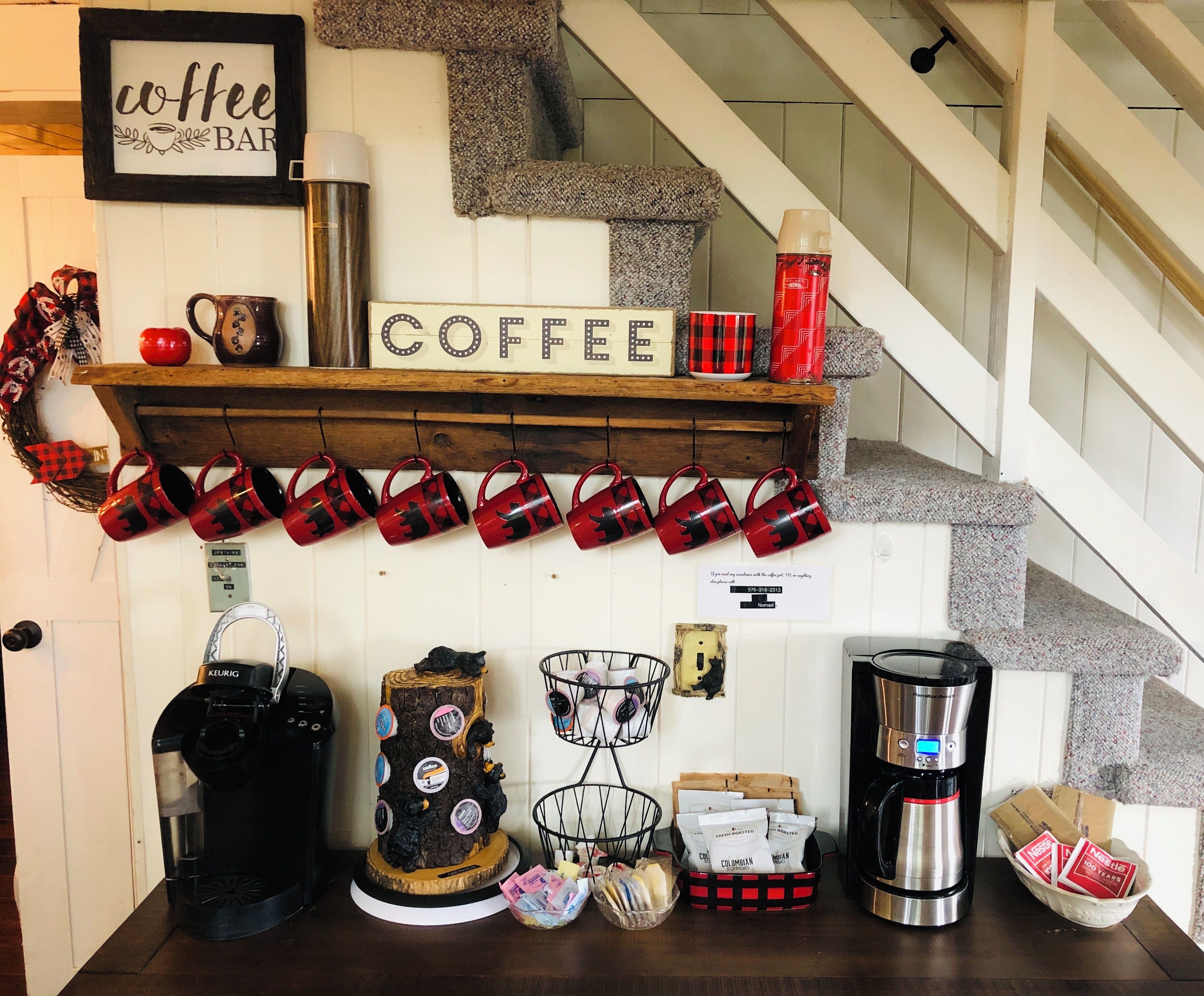 Un comptoir à café avec une enseigne, des tasses, une machine à café et une cafetière.