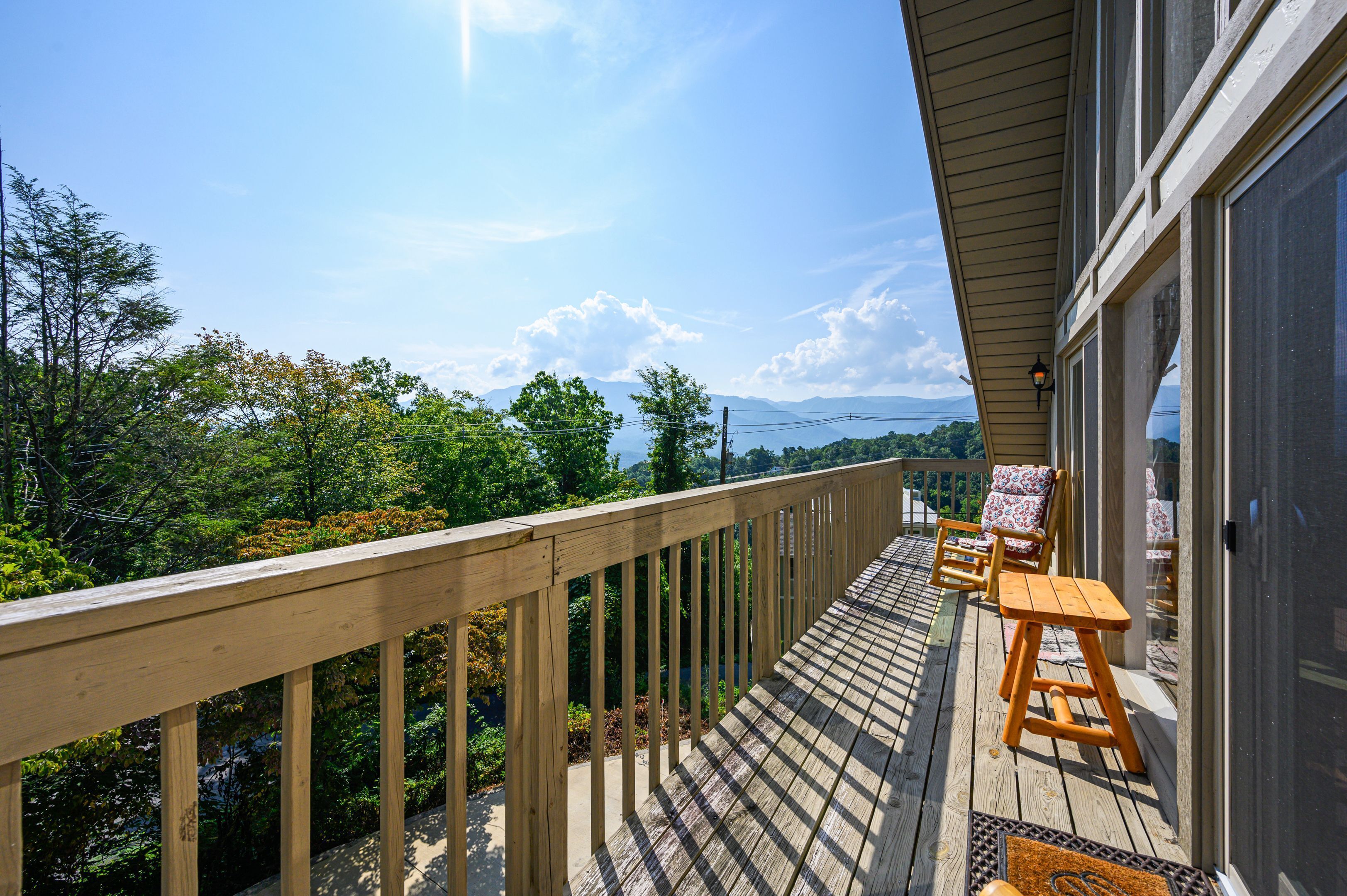 A wooden deck with a view of mountains, a chair, and a table.