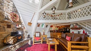 A cozy, rustic interior with a stone fireplace, wooden furniture, and a balcony with a lattice railing. - Mtn VIEWS, 4 bedrooms, hot tub, Arcade games, close to Ober + Gatlinburg (Gatlinburg)