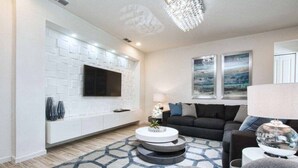 Un salon moderne avec un mur en briques blanches, un téléviseur à écran plat, un canapé noir et un tapis à motifs.