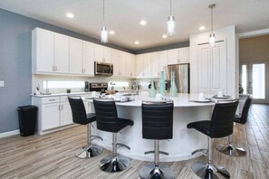 A modern kitchen with white cabinets, a central island with bar stools, stainless steel appliances, and pendant lighting. - Luxury 6BR Disney Villa | Pool, Spa, Game Room, Sleeps 16+1859SN (Kissimmee)