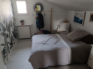 Ein Schlafzimmer mit einem Bett, einem Heizkörper, einem Fenster, einem Spiegel und einer Wand mit tropischem Wandpapier.