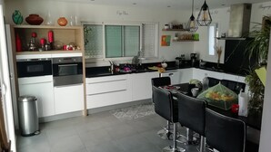 Ett modernt kök med vita skåp, svarta bänkskivor och vitvaror i rostfritt stål. Det finns en matplats med svarta stolar och ett bord, och en papperskorg syns.