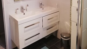 Ett badrum med ett vitt handfat, två tvättställ, en spegel och en hårfön som hänger på väggen.
