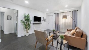Una sala de estar moderna con sofá, sillón, mesa de centro y televisor montado en la pared.