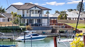 Una casa de dos pisos con un balcón, un muelle con barcos y un cielo despejado.