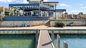 Una casa moderna con un porche cubierto, piscina y muelle de madera.