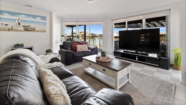 Una sala de estar moderna con un sofá de cuero, una mesa de centro y un televisor de pantalla plana. Una ventana grande ofrece vistas al mar y a barcos.