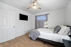 A bedroom with a bed, a ceiling fan, a TV mounted on the wall, and a window with curtains. - Spacious 2 B/R Apt Close to Beach Location! (Lake Worth)