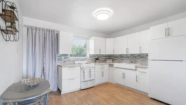 Een moderne keuken met witte kasten, een inbouwoven en een raam met gordijnen.
