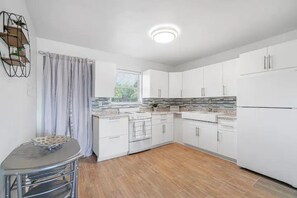 A modern kitchen with white cabinets, a built-in oven, and a window with curtains. - Spacious 2 B/R Apt Close to Beach Location! (Lake Worth)