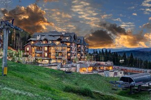 Ein mehrstöckiges Lodge-Gebäude mit Skilift, umgeben von Bergen und einem bewölkten Himmel.