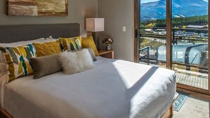 Une chambre dotée d’un grand lit, d’une table de chevet avec une lampe et offrant une vue sur un paysage montagneux grâce à une porte coulissante.
