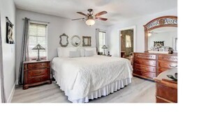 Een slaapkamer met een bed, een dressoir, een spiegel en een plafondventilator.