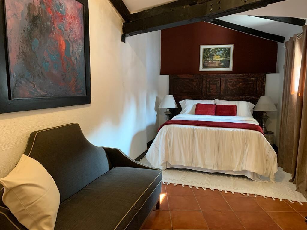 A bedroom with a bed, a sofa, a painting, and a lamp.