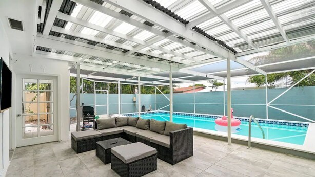 Uma área externa coberta com piscina, sofá modular e churrasqueira.
