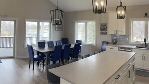 Uma cozinha ampla com uma ilha grande, armários brancos e cadeiras azuis ao redor de uma mesa de jantar.