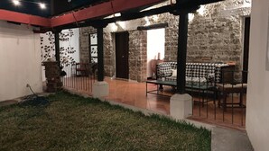 Une cour avec un mur en pierre, un petit jardin et un coin repas agrémenté d’une nappe à motifs.