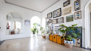 A spacious hallway with a tiled floor, a yellow trunk with a plant, and framed butterfly art on the walls.