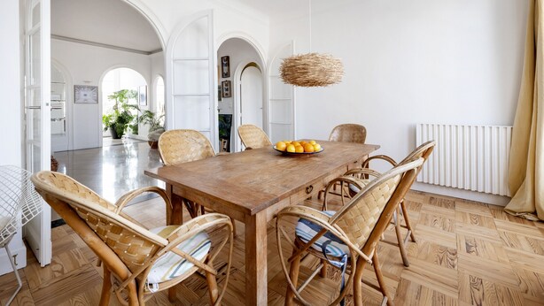 A dining area with a wooden table, wicker chairs, and a fruit bowl.