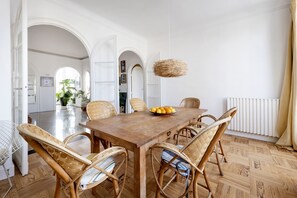 A dining area with a wooden table, wicker chairs, and a fruit bowl.