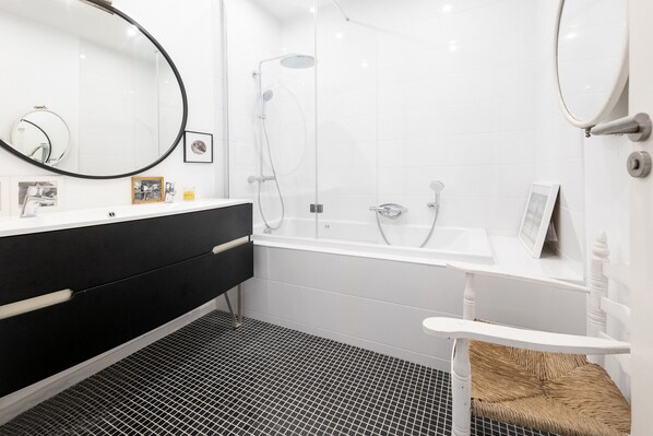 A modern bathroom with a black and white tiled floor, a white sink with a black cabinet, a large mirror, and a shower area.