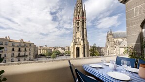 A terrace with a checkered table set for dining, overlooking a historic cathedral with intricate spires.