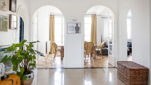 A spacious hallway with white walls, wooden flooring, and a central archway leading to a dining area with wicker chairs and a table.