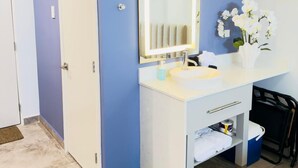 Une salle de bain avec un meuble-lavabo blanc, un miroir, un évier et un vase contenant des fleurs blanches.