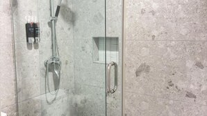 Une douche fermée par des parois en verre, dotée d’un pommeau de douche à main et d’un robinet à main.